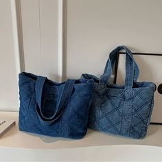 two blue bags sitting on top of a white counter next to a book and phone