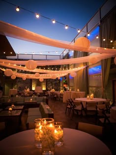 an indoor dining area with tables and chairs covered in white draping at night