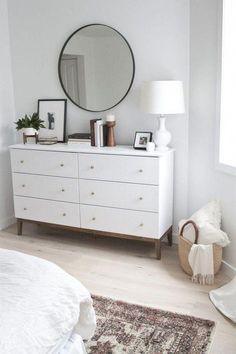 a white dresser sitting next to a mirror on top of a wooden floor in a bedroom