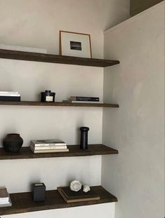 some shelves with books and vases on them in a room that has white walls