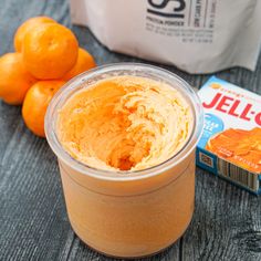 an orange smoothie in a plastic cup next to some oranges and a carton of jello