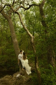 a man and woman standing next to each other in the woods near a river with trees