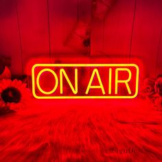 a neon sign that says on air in the middle of a room with sunflowers