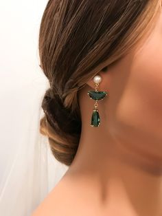 a close up of a woman's head wearing earrings with green stones and pearls