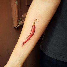 a small red chili pepper tattoo on the left inner arm and forearm, with a yellow tip