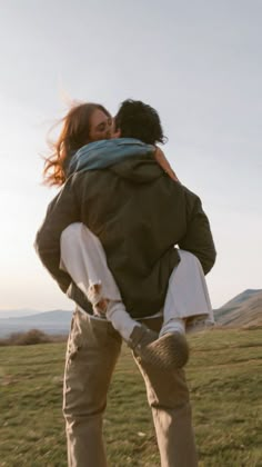 two people standing in the grass with one holding the other's back as they hug