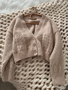 a cardigan sweater is laying on top of a knitted blanket with a wooden hanger