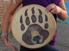 a woman holding a drum with a bear paw painted on it