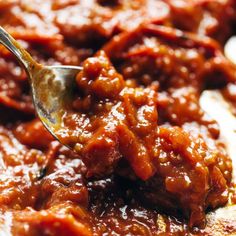 a spoon is being used to scoop chili out of the pot with meat in it