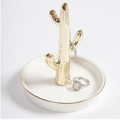 a gold cactus ring holder on a white plate with a diamond in the middle,