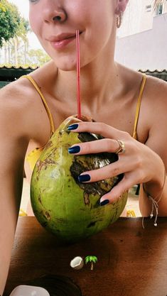 a woman drinking from a straw in front of a green coconut