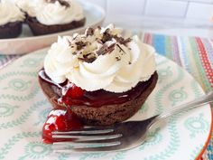 a chocolate cupcake with whipped cream and cherries on top is sitting on a plate next to a fork