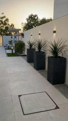 three black planters sitting on the side of a white wall next to a sidewalk