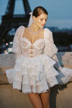 a woman standing in front of the eiffel tower wearing a white wedding dress