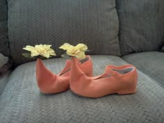 two orange shoes sitting on top of a couch next to each other with yellow flowers in them