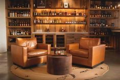 two leather chairs sitting in front of a wooden shelf filled with bottles and liquors