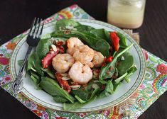 a plate with spinach and shrimp on it next to a glass of orange juice