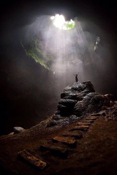 a person standing at the end of a tunnel with light coming from behind it and on top of some rocks