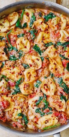 a pan filled with pasta and spinach on top of a wooden table next to utensils