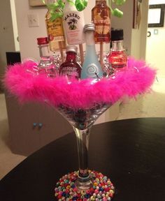 a martini glass filled with liquor bottles and pink feathers sitting on top of a table