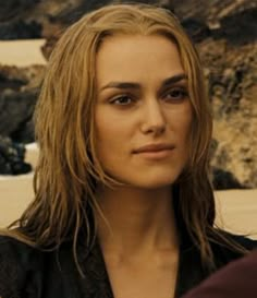 a close up of a person wearing a black shirt and long blonde hair with rocks in the background