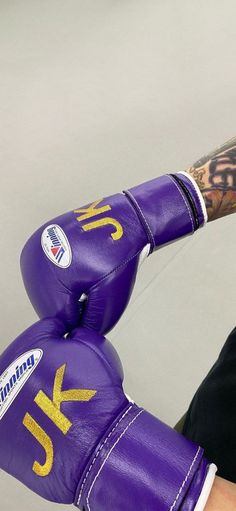 a close up of a person wearing purple boxing gloves with gold letters on them,