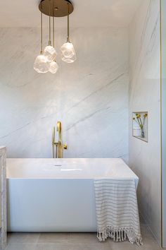 a white bath tub sitting next to a bathroom sink under a light hanging above it