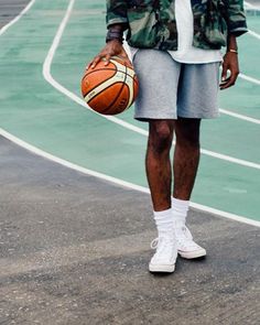 a man holding a basketball while standing on top of a basketball court with his hands in his pockets