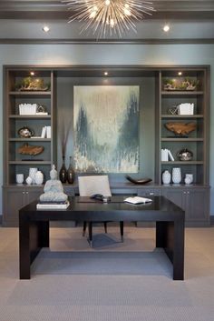 an office with two desks and bookshelves on the wall, in front of a large painting