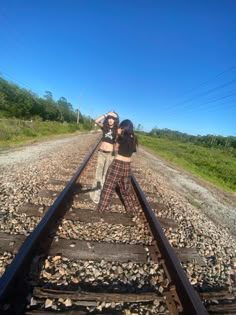 two people standing on train tracks with their arms around each other's backs, one person taking a selfie