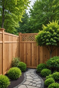 a wooden fence surrounded by green trees and shrubbery with a stone path leading to it