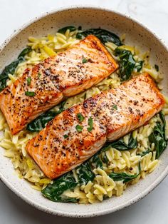 two salmon fillets with pasta and spinach in a white bowl on a marble surface