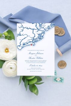 the wedding stationery is laid out on top of blue satin and flowers, with two coins