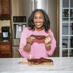 a woman is holding up some ribs on a cutting board in front of an oven