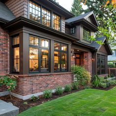 a large brick house with lots of windows on the front and side of it, surrounded by lush green grass