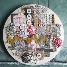 a white circular wall hanging with buttons and other things on it, in front of a green painted wall