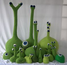 a group of green stuffed animals sitting next to each other on a white cloth covered surface