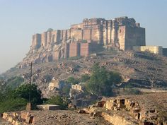 an old castle sits on top of a rocky hill with trees in the foreground