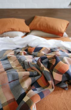 an unmade bed with orange and blue plaid blankets on it, along with two pillows