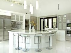 a large white kitchen with lots of counter space and stools around the center island