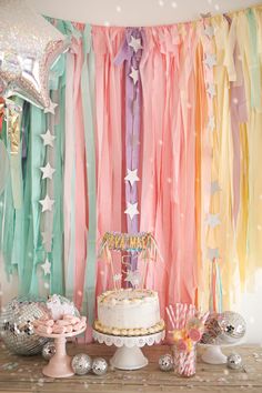 a birthday party with cake, balloons and streamers in pastel colors on a wooden table