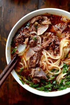 a bowl of beef and noodle soup with chopsticks on the side, ready to be eaten