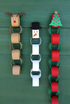 paper roll snowman and reindeer decorations hanging on a green wooden wall with red ribbon