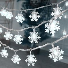 white snowflakes are hanging on a string in front of a christmas tree with lights