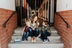 a woman and two boys sitting on the steps with books in front of their faces