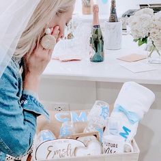 a woman sitting in front of a table holding a cell phone to her ear, next to a basket filled with personal care items