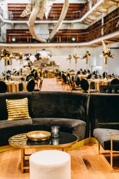 a room filled with black couches and tables covered in gold cloth centerpieces