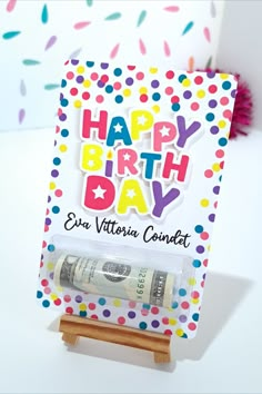 a happy birthday card with money and confetti on it, sitting on a small wooden easer