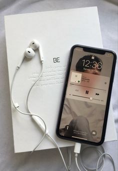 an iphone with ear buds and headphones on top of a piece of white paper