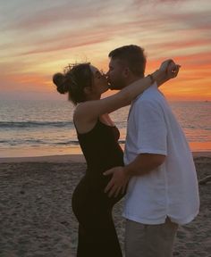 a pregnant couple kissing on the beach at sunset